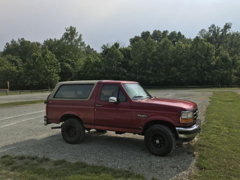 1994 Ford Bronco - This Ford Bronco is parked on a gravel lot with a line of trees behind it.