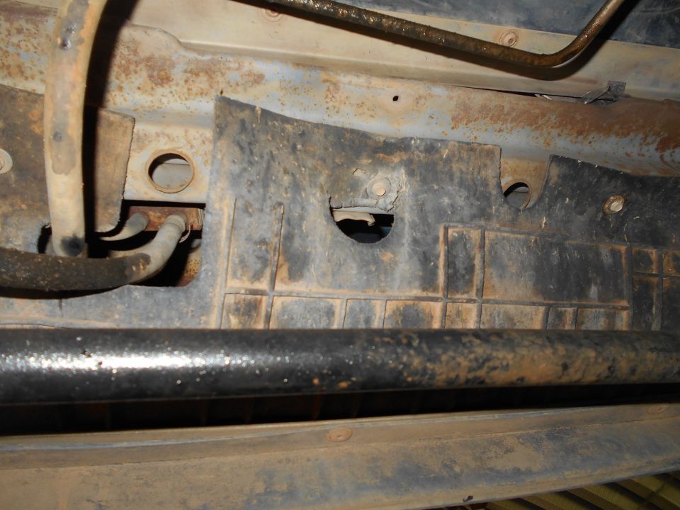 Underside of vehicle showing rusty frame, fuel lines, and a black plastic shield