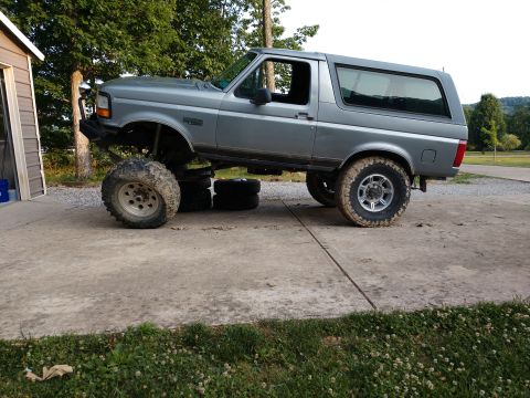 1995 Ford Bronco - A lifted gray Ford Bronco sits on a concrete pad, its front tires elevated by stacked spare tires.