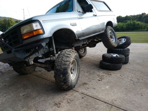 1995 Ford Bronco - Silver 1995 Ford Bronco with large off-road tires is shown with its front driver's side wheel elevated on a stack of tires.