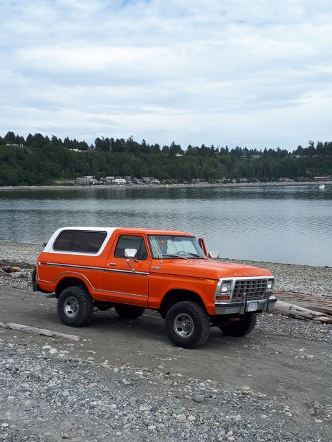 1978 Ford Bronco - This 1978 Ford Bronco is parked on a beach with a wooded hillside and water in the background.