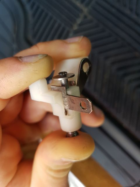 1978 Ford Bronco - Close-up of a white plastic automotive part with metal contacts being held by fingers.