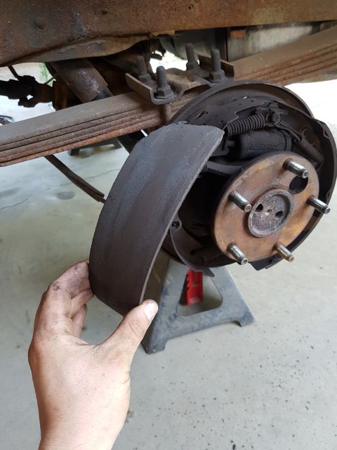 1978 Ford Bronco - A detached brake shoe is held up to the brake drum assembly, showing wear and tear on the vehicle's rear axle.