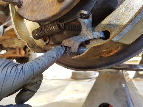 1978 Ford Bronco - A gloved hand points to a part of the brake drum assembly, likely during maintenance or repair.