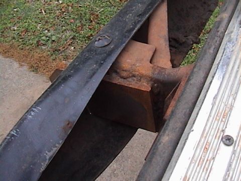 1978 Ford Bronco - Close-up looking down between the rear frame rail and body of a truck at a rusty fabricated steel bracket welded in place, with a black rea…