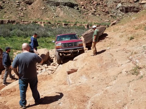 1995 Ford Bronco - A red Ford F-150 is being driven on a challenging off-road trail with several people observing the action.