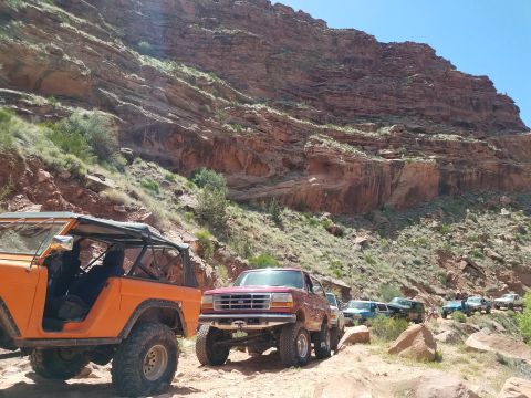1995 Ford Bronco - A convoy of SUVs navigates a canyon trail under a clear blue sky.