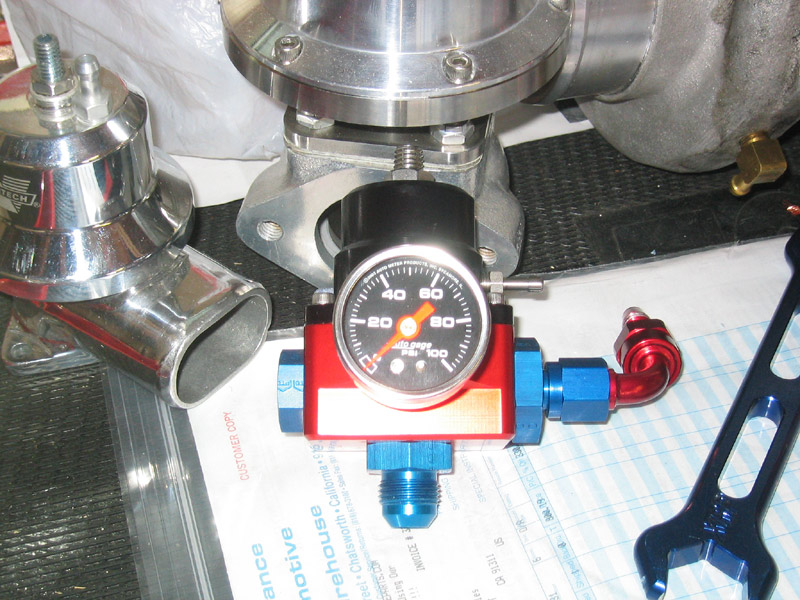 Chrome blow-off valve, red fuel pressure regulator with gauge, and a black wrench on a document
