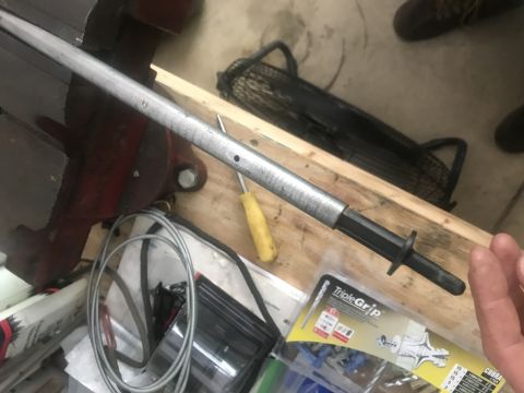 1994 Ford Bronco - A metal rod with a black handle is clamped in a vise. A yellow screwdriver and a coiled cable are visible nearby.
