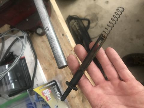 1994 Ford Bronco - A hand holds a disassembled metal and plastic component with a coiled spring. In the background, a metal pipe is held in a vise.