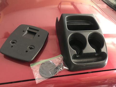 1994 Ford Bronco - Two black plastic automotive interior parts are displayed on a red surface. On the left is a flat rectangular piece with mounting points, a…