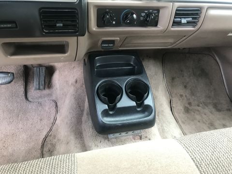1994 Ford Bronco - The interior of a vehicle shows the center console area with cup holders and a power point. The dashboard above features climate controls a…