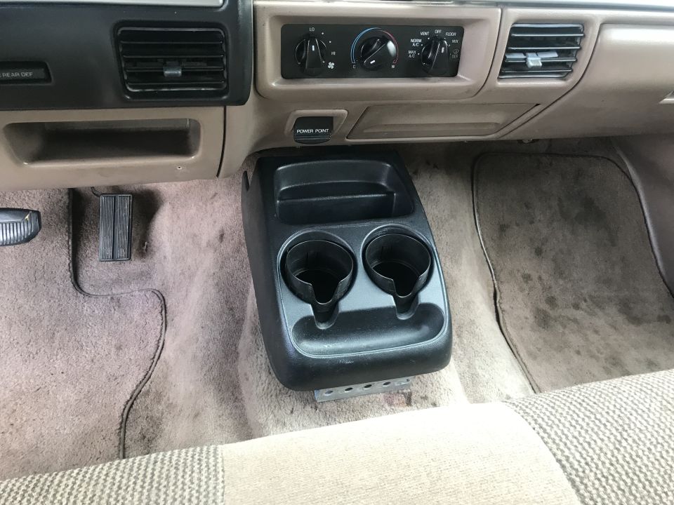Interior view of a vehicle's center console and dashboard with cup holders and climate controls.