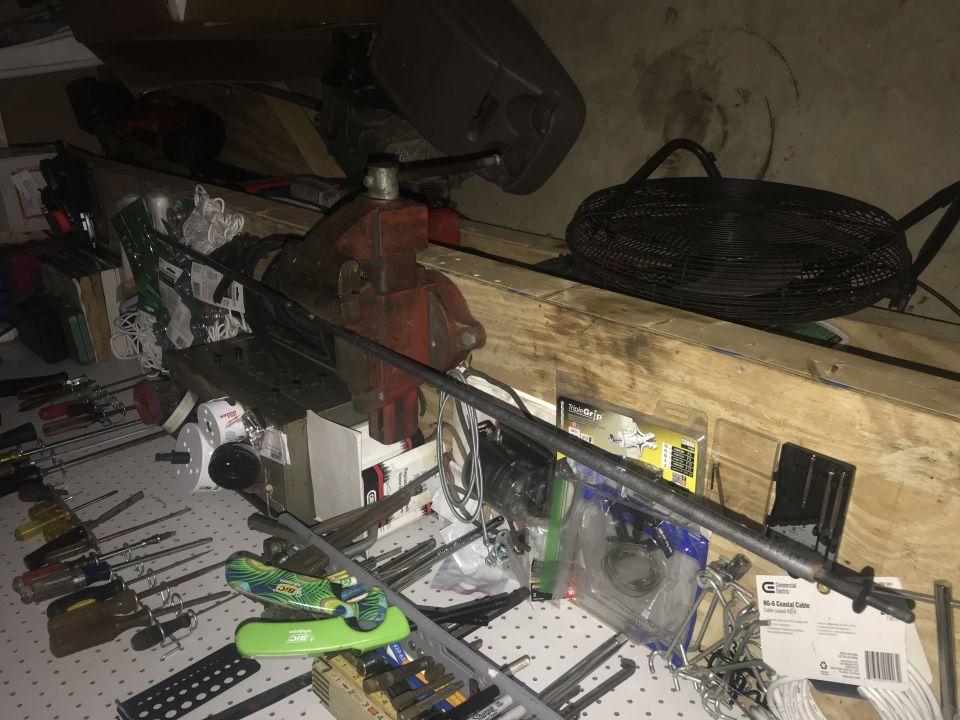 Workbench cluttered with tools, vise, screwdrivers, and fan.
