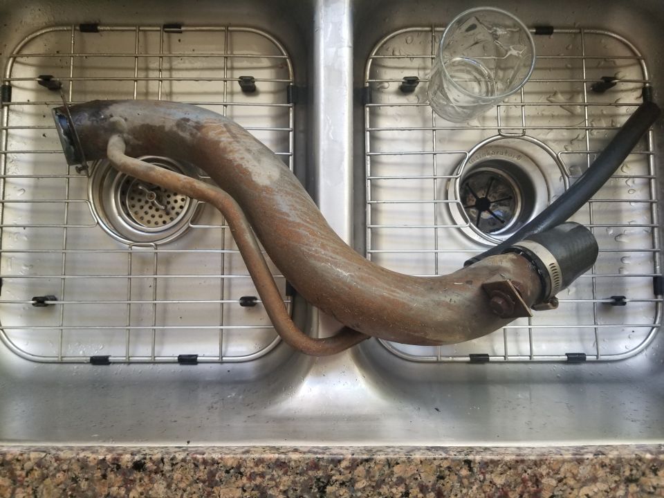 Rusty exhaust pipe with hose in a kitchen sink.
