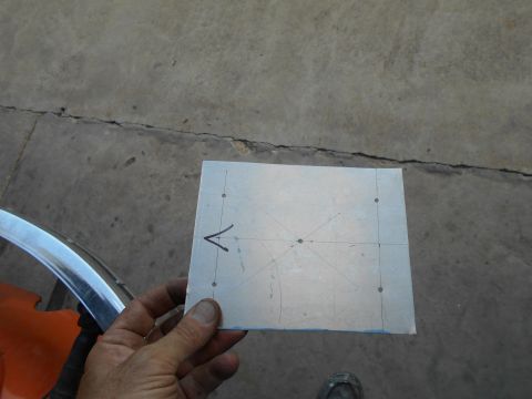 1992 Ford Bronco - A hand holds a piece of metal with markings and drilled holes, likely for a project. The metal is placed on a concrete surface.