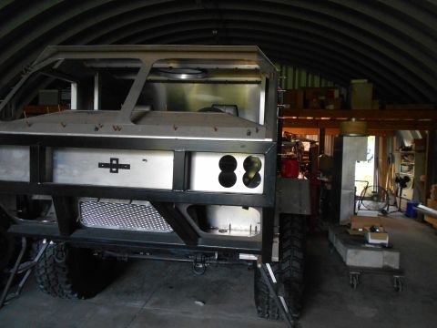1992 Ford Bronco - A custom-built vehicle frame with a metal body is shown in a workshop setting. The front of the vehicle features a black bumper with a silv…