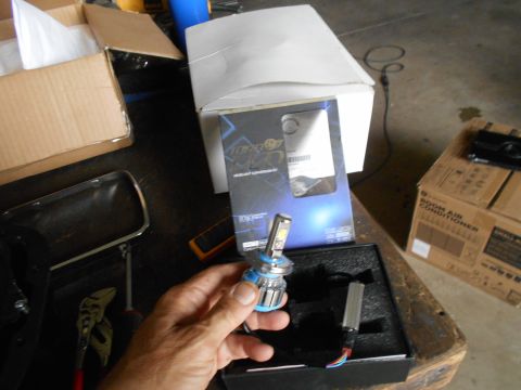 1992 Ford Bronco - A person is holding a new LED headlight bulb over an open box containing another LED bulb and its wiring. In the background are several car…