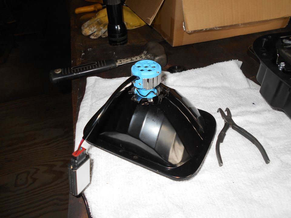 Black headlight assembly with blue LED bulb, wiring harness, and pliers on a white towel.