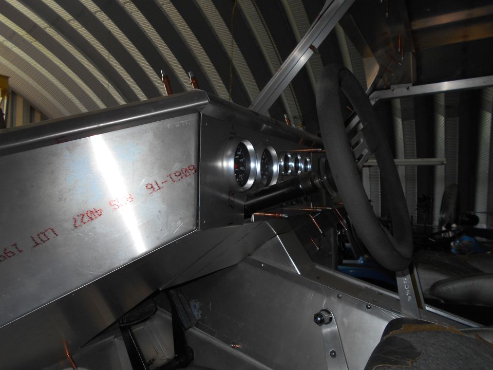 Interior of a custom vehicle with aluminum dashboard, gauges, and steering wheel.