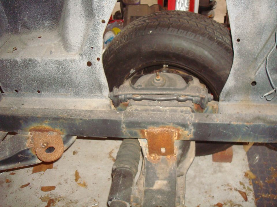 Underside of a vehicle chassis with spare tire and rusty frame.