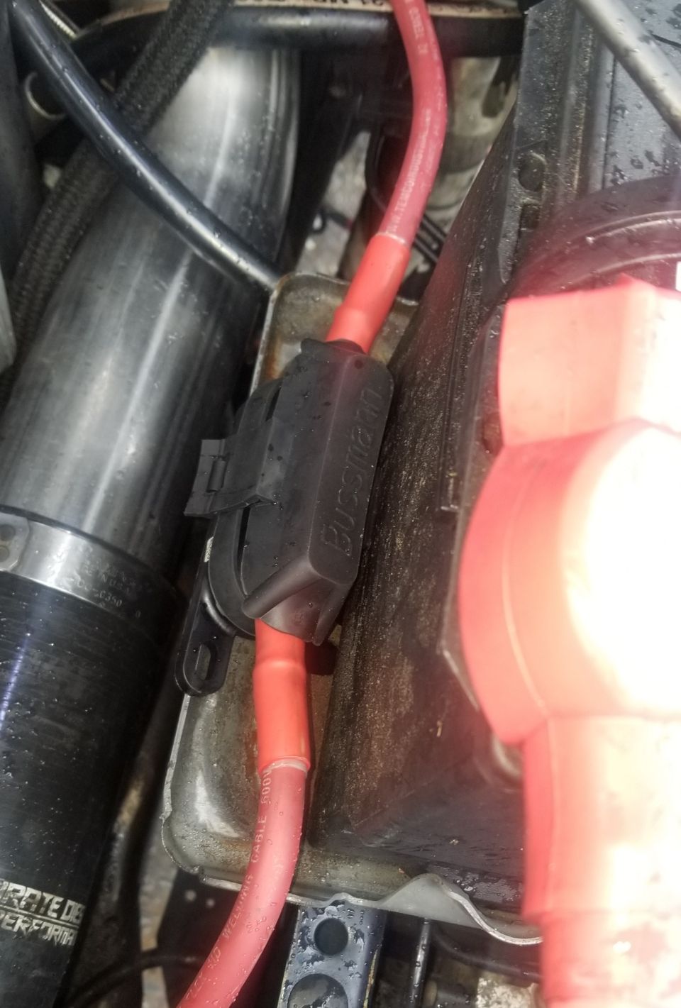 Close-up of a red automotive cable and Bussmann fuse holder near a battery terminal.