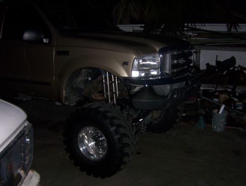 2000 Ford F-450 - Night shot of a gold Ford Super Duty pickup parked in a carport, lifted high on huge bar-tread military-style tires and polished dual-ring…