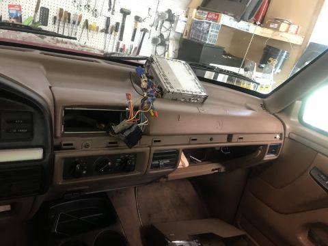 1994 Ford Bronco - The interior of a vintage Ford Bronco's dashboard is shown with the radio removed and wires exposed. Various tools are visible on a pegboar…