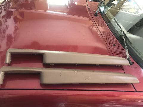 1994 Ford Bronco - Two tan interior trim pieces are laid out on the red hood of a vehicle. The pieces appear to be door panel or dashboard trim.