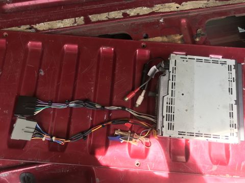 1994 Ford Bronco - The back of a red vehicle bed shows a disassembled car stereo with its wiring harness and RCA cables. The stereo unit is silver and has ven…