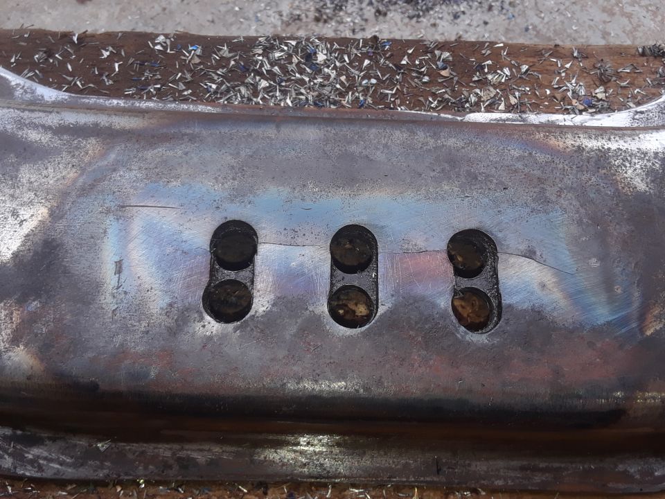 Metal part with three pairs of holes, showing heat discoloration and a crack.