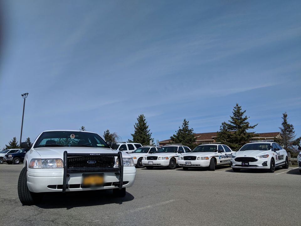 Ford Crown Victoria police car with push bumper in foreground, several other police sedans and an SUV parked behind it