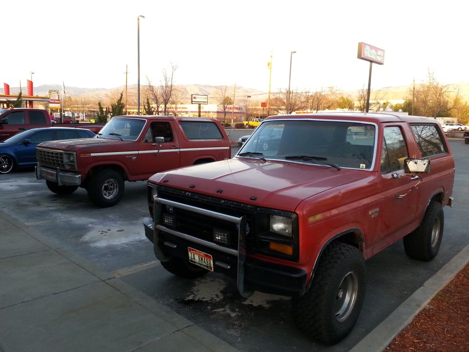 Two red Ford Broncos parked in a lot, one with a custom bumper and license plate.