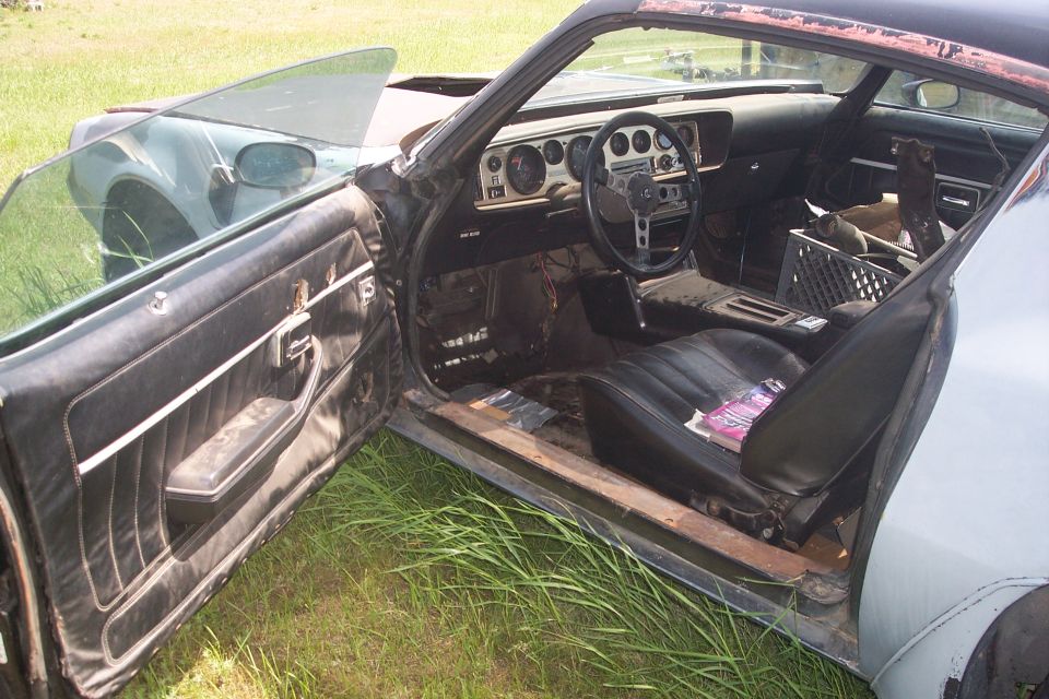 Interior of a classic car with the driver's door open, showing worn seats, dashboard, and steering wheel.