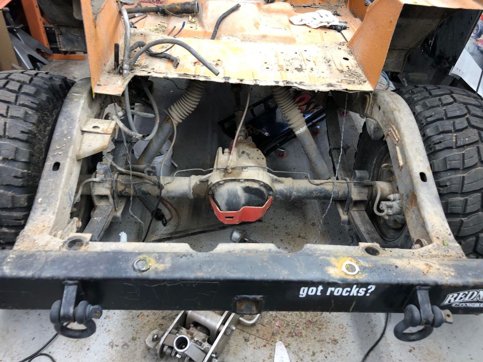 Rear axle and suspension of an orange Jeep Wrangler with a black bumper that says "got rocks?"