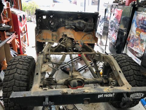1992 Jeep Wrangler - The chassis and drivetrain of a Jeep Wrangler are shown in a garage setting, with large off-road tires mounted. The frame has the text "got…
