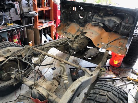 1992 Jeep Wrangler - The partially disassembled chassis of an orange Jeep Wrangler sits in a garage, with the engine and drivetrain exposed. Various tools and e…