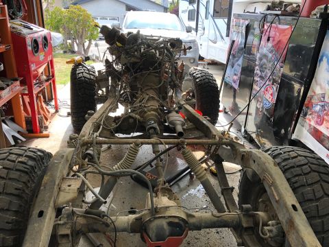 1992 Jeep Wrangler - The chassis and drivetrain of a Jeep Wrangler are shown in a garage setting. The vehicle is partially disassembled with the engine and tran…