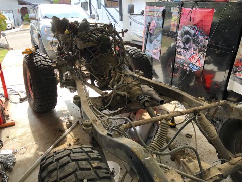 1992 Jeep Wrangler - The frame and drivetrain of a disassembled Jeep Wrangler are shown in a garage setting. Large off-road tires and various mechanical compone…