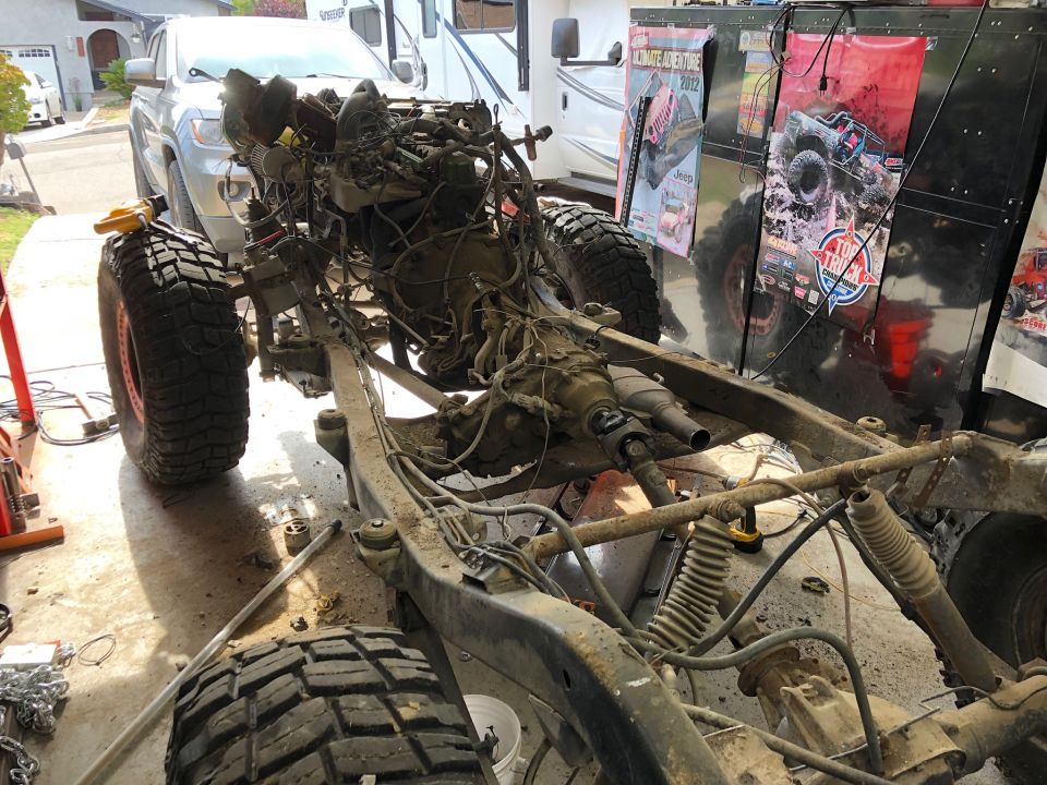 Disassembled 1992 Jeep Wrangler frame with drivetrain, large tires, and engine components in a garage.