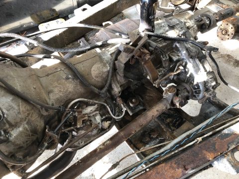 1992 Jeep Wrangler - A close-up view of a dirty and greasy vehicle transmission and transfer case assembly, with drive shafts attached. Various wires and hoses…