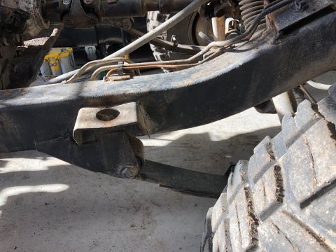 1992 Jeep Wrangler - A close-up view of the rusted frame and suspension components of a vehicle, including a leaf spring and a tire. Metal brake lines are also…