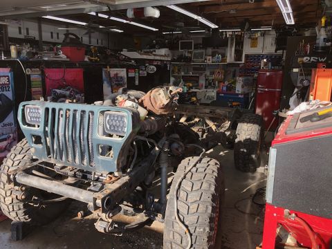 1992 Jeep Wrangler - A partially disassembled Jeep Wrangler is in a garage, showing its front grille, headlights, and large off-road tires. The vehicle is under…