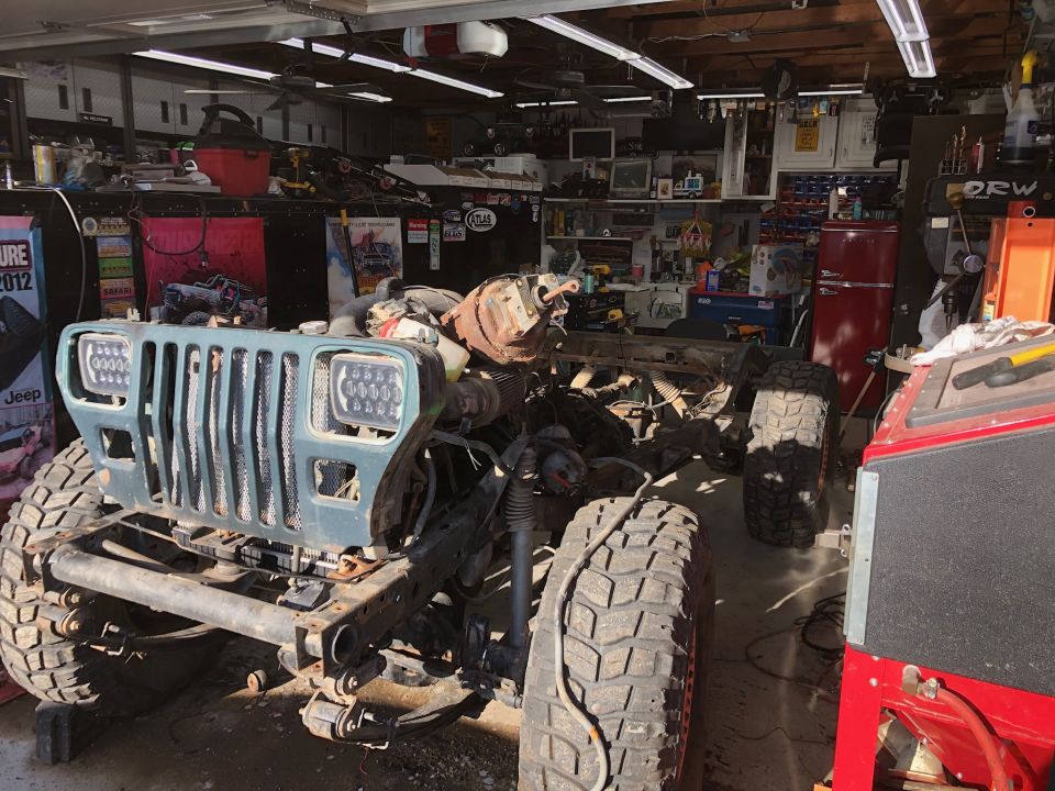 Jeep Wrangler front end with large tires, partially disassembled in a garage.