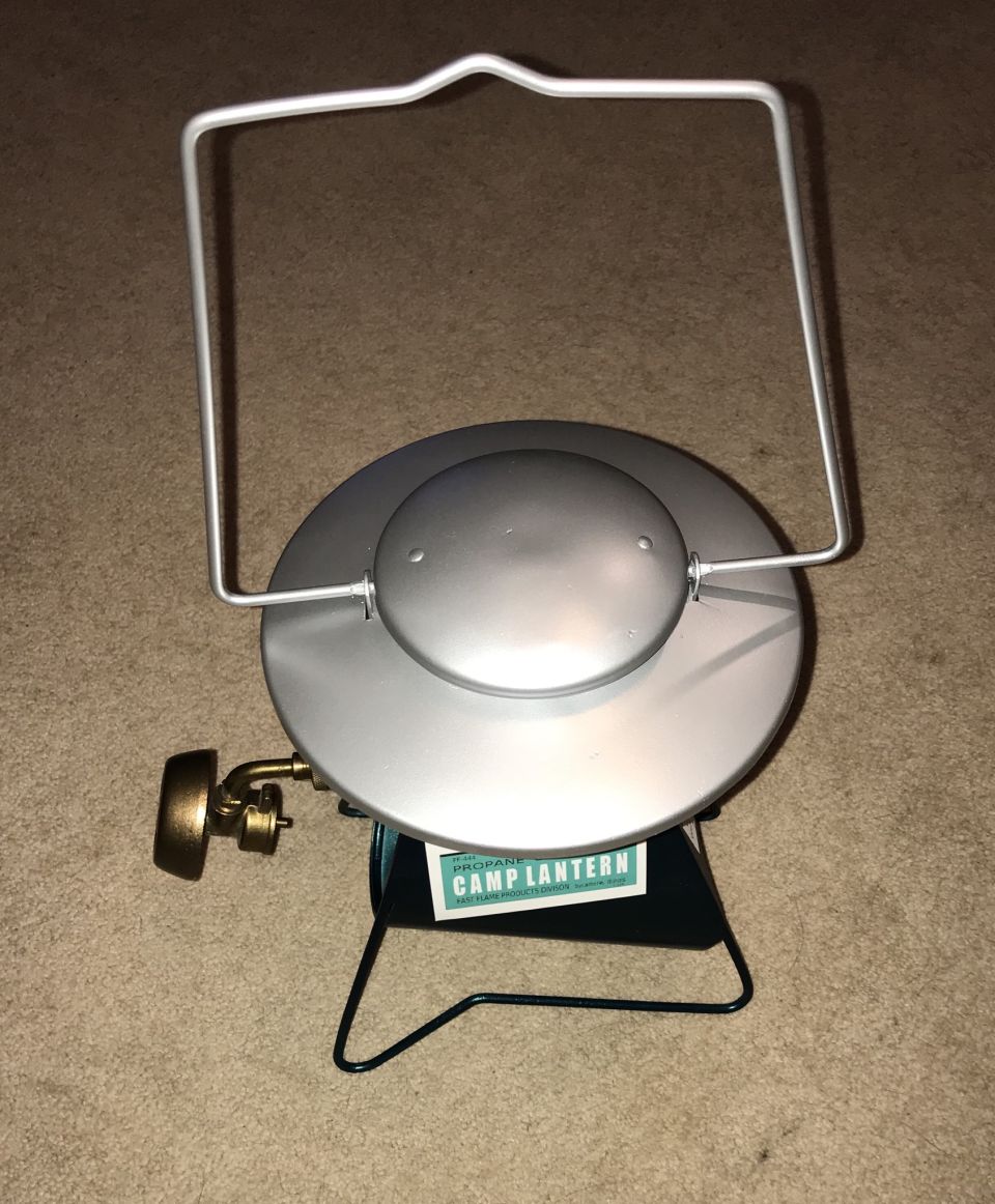 Propane camp lantern with silver top and green base on carpet.