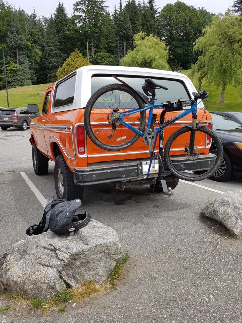 1978 Ford Bronco - An orange 1978 Ford Bronco is parked in a lot with a blue mountain bike mounted on a rear rack. A black full-face helmet rests on a large r…