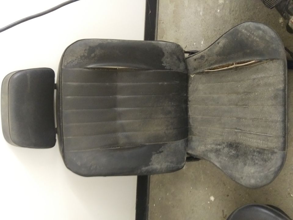 Worn black car seat with headrest, showing fabric damage.