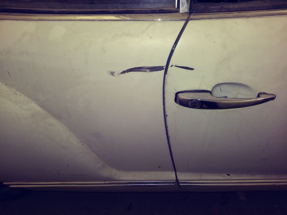 White vintage car door with chrome handle, showing scratches and cracks.