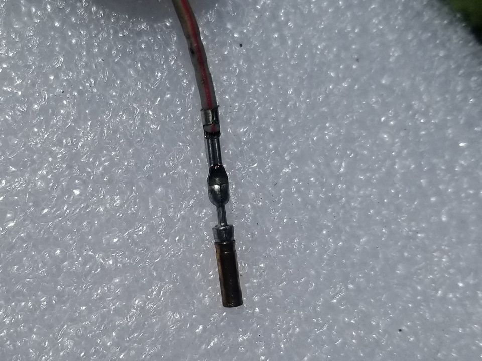 Crimped electrical connector on a wire with red and white insulation.