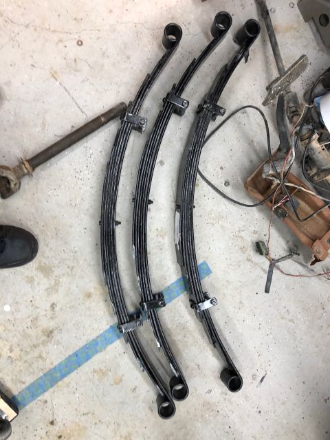1992 Jeep Wrangler - Three black leaf springs are laid out on a concrete floor, with a metal shaft extending from the left side of the frame.